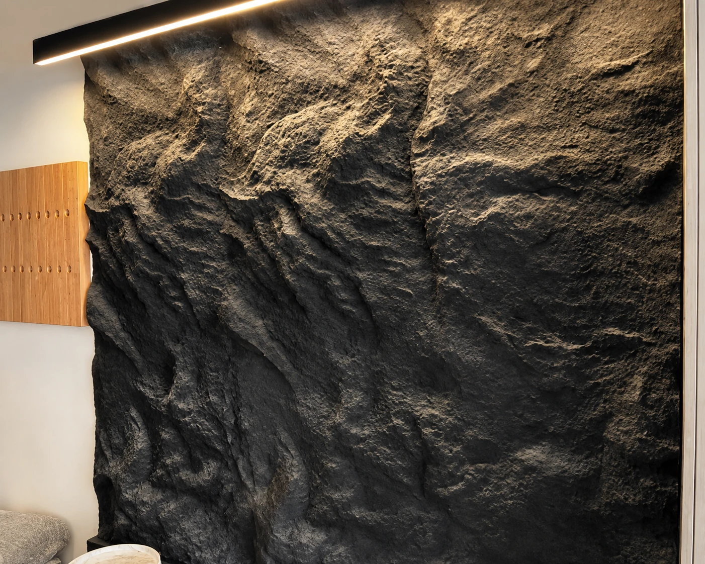 Charcoal rock texture feature wall highlighted by linear lighting